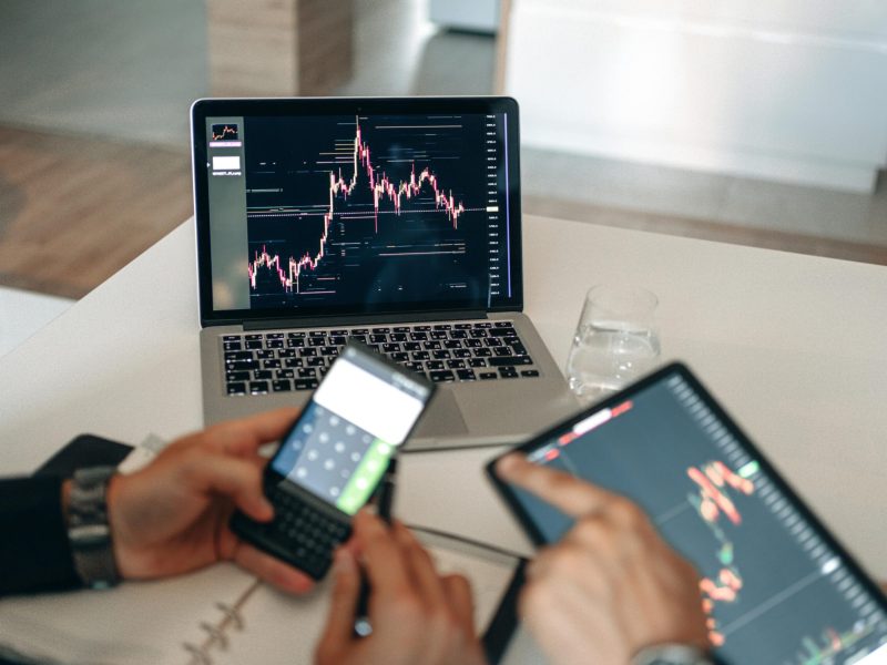 Hands using digital devices for financial analysis at a modern desk setup.